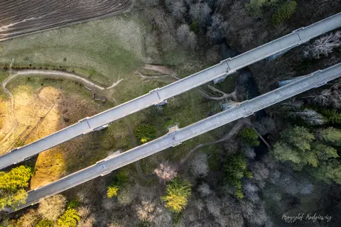 Dwa równoległe wiadukty przecinają leśną dolinę, oglądane pionowo z góry.