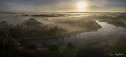 Poranna mgła unosi się nad lasem i zakolem rzeki w złotym świetle.
