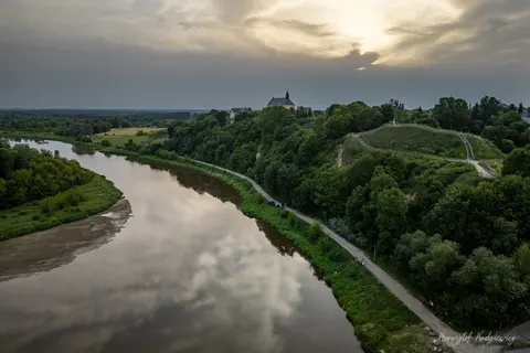 Spokojny nurt rzeki prowadzi w stronę wzgórza z zabytkową budowlą.