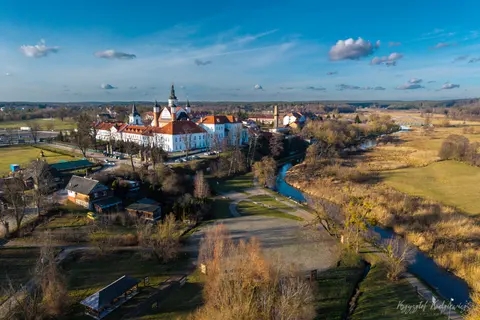 Jasna świątynia nad krętą rzeką na tle otwartych łąk i pól.