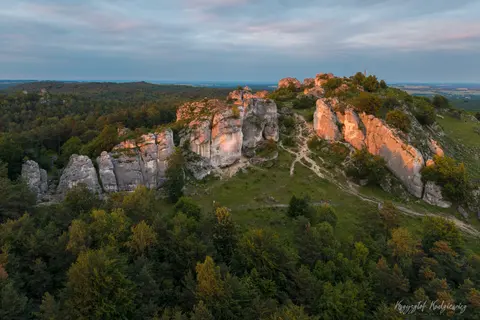 Wieczorne słońce wydobywa ciepłe barwy skalnych ścian ponad zielonym lasem.