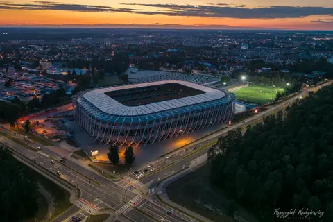 Oświetlony stadion na tle miasta i ostatniego pomarańczowego światła na horyzoncie.