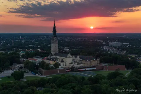Słońce zachodzi za miastem, podkreślając sylwetkę wysokiej wieży i dawnych murów.