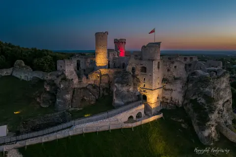 Podświetlone zamkowe ruiny i drewniany most na tle granatowego nieba.
