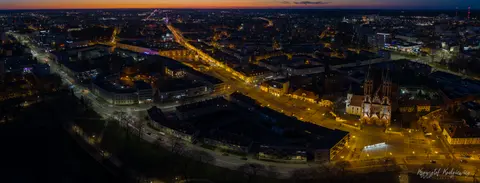 Panorama miasta po zmroku, z jasną osią głównej ulicy i katedralnymi wieżami.