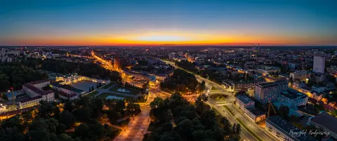 Miejskie arterie rysują świetliste linie pod pomarańczowym pasmem wieczornego nieba.