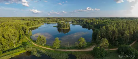 Zakole wody otoczone lasem i łąkami w jasnym, zielonym krajobrazie.