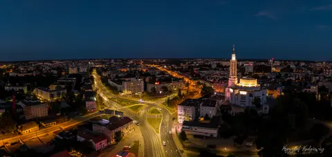Rozświetlona wieża i zbiegające się ulice na tle granatowej panoramy miasta.