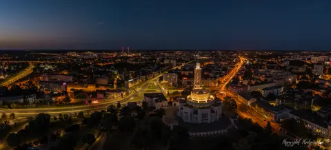 Panorama nocnego miasta z podświetloną wieżą na pierwszym planie.