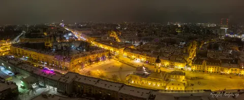 Długi miejski plac i jasne fasady kamienic w świetle nocnych latarni.