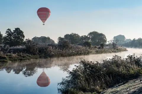 Kolorowy balon i jego odbicie unoszą się nad zamglonym zakolem rzeki.