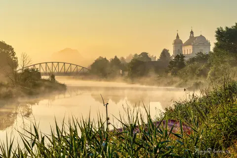 Poranna mgła otula rzekę, most i świątynię stojącą na wysokim brzegu.