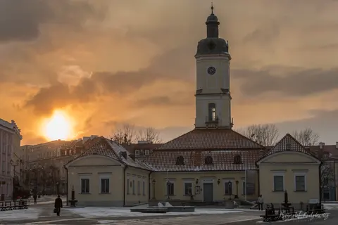 Niskie słońce i ciepła poświata otaczają jasny ratusz z wysoką wieżą.