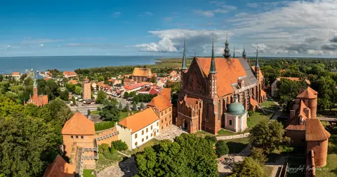 Strzeliste dachy ceglanego zespołu zamkowego górują nad zielenią i zabudową miasta.