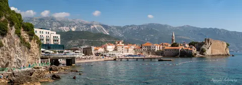 Nadmorskie mury i dachy starego miasta na tle wysokich, skalistych gór.
