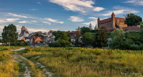 Ceglany zamek i dachy miasteczka wyłaniają się zza zielonych nadrzecznych łąk.