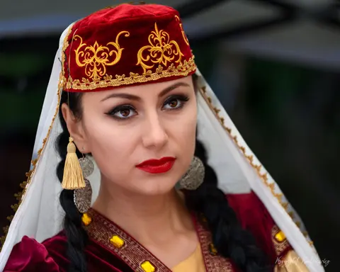 Portret kobiety w czerwonym nakryciu głowy, z haftem, welonem i długimi kolczykami.