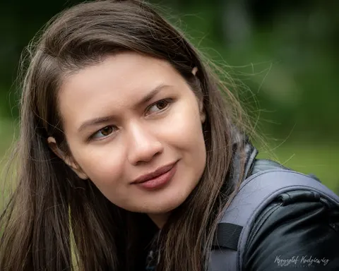 Młoda kobieta spogląda w bok na miękko rozmytym, zielonym tle.