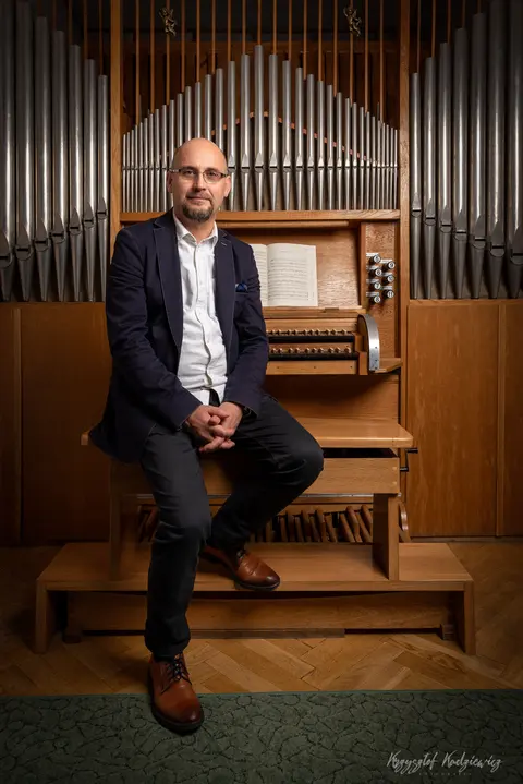 Portret mężczyzny siedzącego przy organach w ciepłym świetle drewnianego wnętrza.