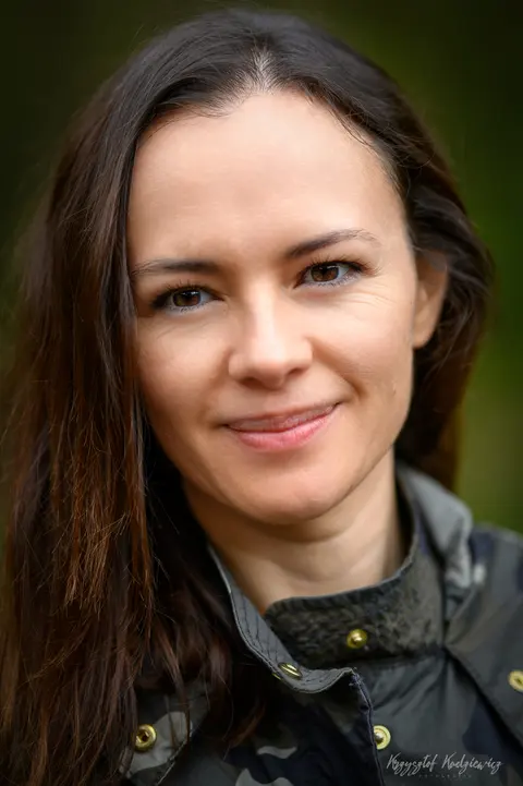 Delikatny uśmiech i bezpośrednie spojrzenie w naturalnym portrecie na zielonym tle.