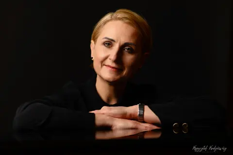 Uśmiechnięta kobieta opiera ramiona na lśniącej powierzchni, która odbija jej dłonie.