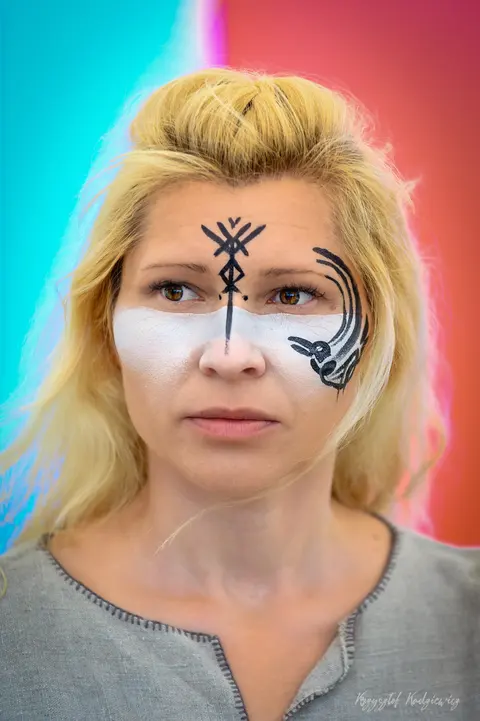 Kobieta z czarnym, geometrycznym malunkiem na twarzy w jasnym, plenerowym portrecie.