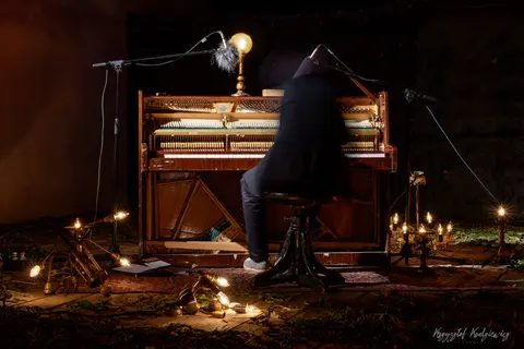 Pianista przy odsłoniętym pianinie, otoczony świecami i ciepłym, punktowym światłem.