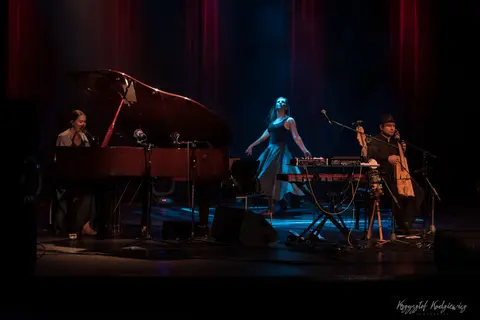 Fortepian, mikrofony i instrumenty klawiszowe tworzą kameralną scenę w czerwonym świetle.