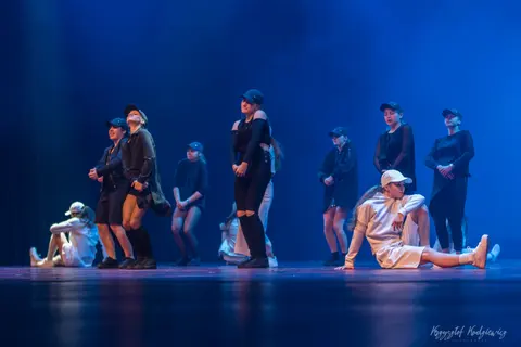 Tancerze w kaszkietach i strojach scenicznych zatrzymani w różnych pozycjach choreografii.