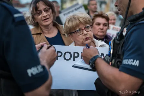 Uczestniczki zgromadzenia rozmawiają z policjantami, trzymając biały transparent.