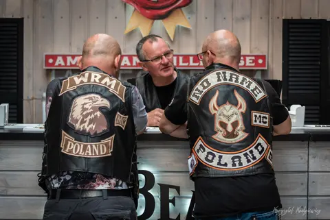 Rozmowa przy kontuarze pomiędzy motocyklistami w skórzanych kamizelkach z naszywkami.