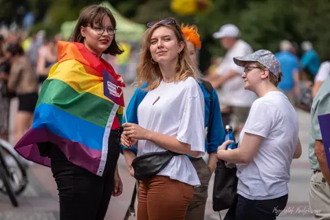 Osoby z tęczową flagą rozmawiają wśród uczestników ulicznego zgromadzenia.