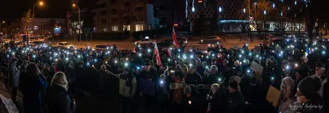 Światła telefonów rozświetlają tłum zgromadzony na miejskim placu po zmroku.