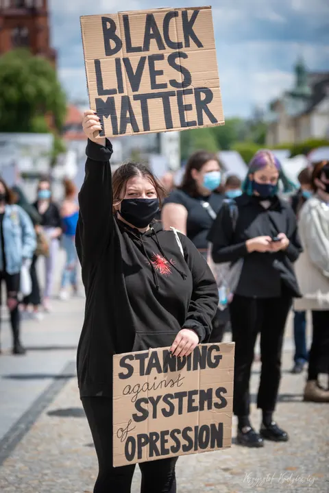 Transparent „Black Lives Matter” unosi się ponad osobami w maseczkach na ulicznym zgromadzeniu.