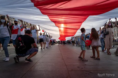 Uczestnicy przemarszu podtrzymują wielką tkaninę z szerokimi białymi i czerwonymi pasami.