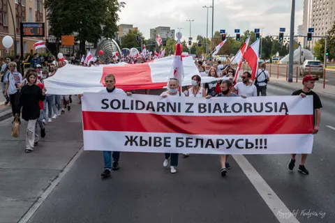 Uliczny pochód niesie biało-czerwono-biały transparent z napisem „Solidarni z Białorusią”.