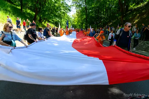 Uczestnicy niosą ogromną biało-czerwoną flagę przez parkową aleję.
